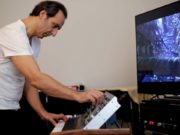 A man playing a MatrixBrute keyboard in front of a tv.