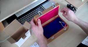 A person is opening a wooden box on a desk.